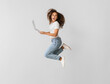 Young woman with laptop jumping on light background