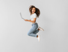 Young Woman With Laptop Jumping On Light Background