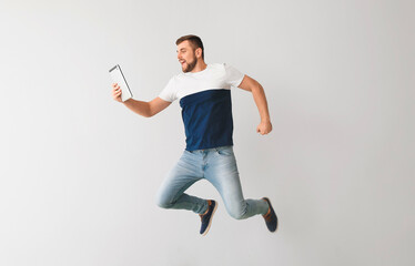 Wall Mural - Young man with tablet computer jumping on light background