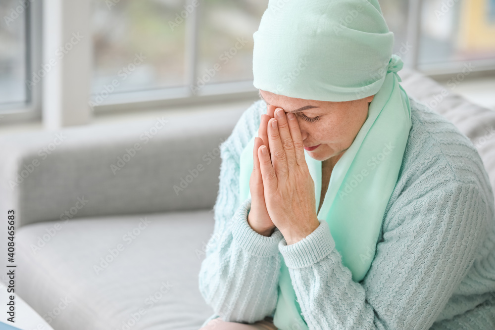 Mature woman praying after chemotherapy at home
