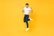 Happy Energetic Young Asian Man Jumping Yelling And Clenching Fists Isolated On Yellow Studio Background