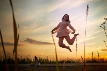 Beautiful sexy girl in pink dress jumping on the asphalt highway during sunset and field with grass on the side of the road