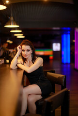 Beautiful brunette woman in evening dress posing near bar alone