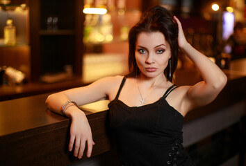Beautiful brunette woman in evening dress posing near bar alone