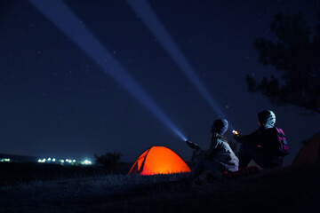 couple with flashlights near camping tent outdoors at night