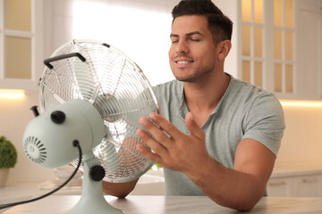 Wall Mural - Man enjoying air flow from fan at table in kitchen. Summer heat