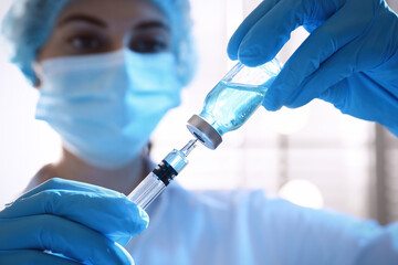 Poster - Woman filling syringe with vaccine from vial on blurred background, closeup