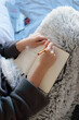 © Edgar - Mujer joven caucásica escribiendo en una libreta con un lápiz encima de la falda tapada con una manta. Estudiar en casa
