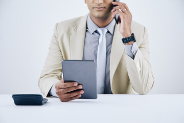 Wall Mural - cropped image of serious young businessman reading e-mail on tablet computer and talking on phone wi