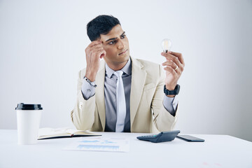 Wall Mural - portrait of pensive young asian entrepreneur looking at lightbulb in his hand and looking for inspir