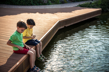 Wall Mural - Two children feed the wild ducks and shoal of small fish in azure clean transparent lake. Brother boys are best friends. Summer holiday friendship concept