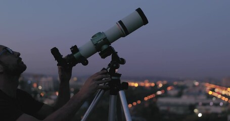 amateur astronomer looking at the stars with a telescope with blurred city lights in the background.