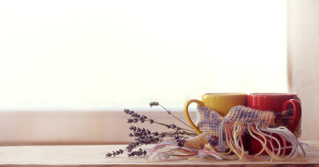 Wall Mural - red and yellow cups are wrapped in a purple scarf and decorated with a lavender bouquet against the background of the window. date with the aroma of coffee