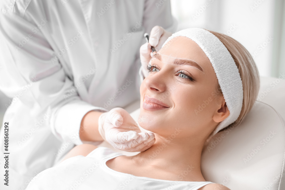 Young woman undergoing eyebrow correction procedure in beauty salon