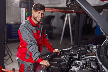 Cheerful technician repairing car in garage