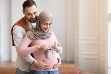 Wall Mural - Muslim Husband Holding Tiny Shoes Hugging Pregnant Wife's Belly Indoor