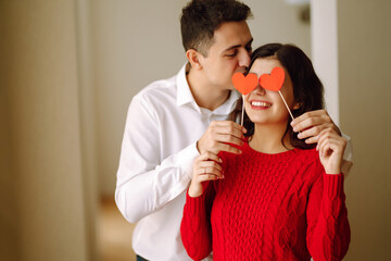 Wall Mural - Happy couple huging and holding red hearts over eyes. Valentine’s Day, celebration, love and romance.