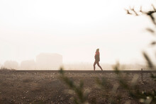 Thoughtful Woman Walking On A Foggy Railroad While Looking Away