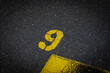 © YK - Grey asphalt road, yellow painted number nine on grey street, yellow lines like a corner on the road, space for text