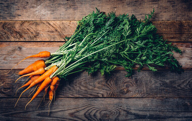 Fresh organic carrots with green leaves on wooden background. Vegetables. Healthy food. Top view, toned