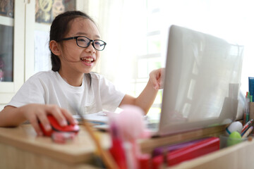 Cheerful young little Asian girl teenage using laptop computer at home during the pandemic lockdown, Homeschooling and online e-learning at home concept.