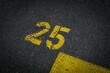 © YK - Grey asphalt road, yellow painted number twenty five on grey street, yellow lines like a corner on the road, space for text