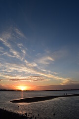 two distant people silhouetted on a sand island at sunset