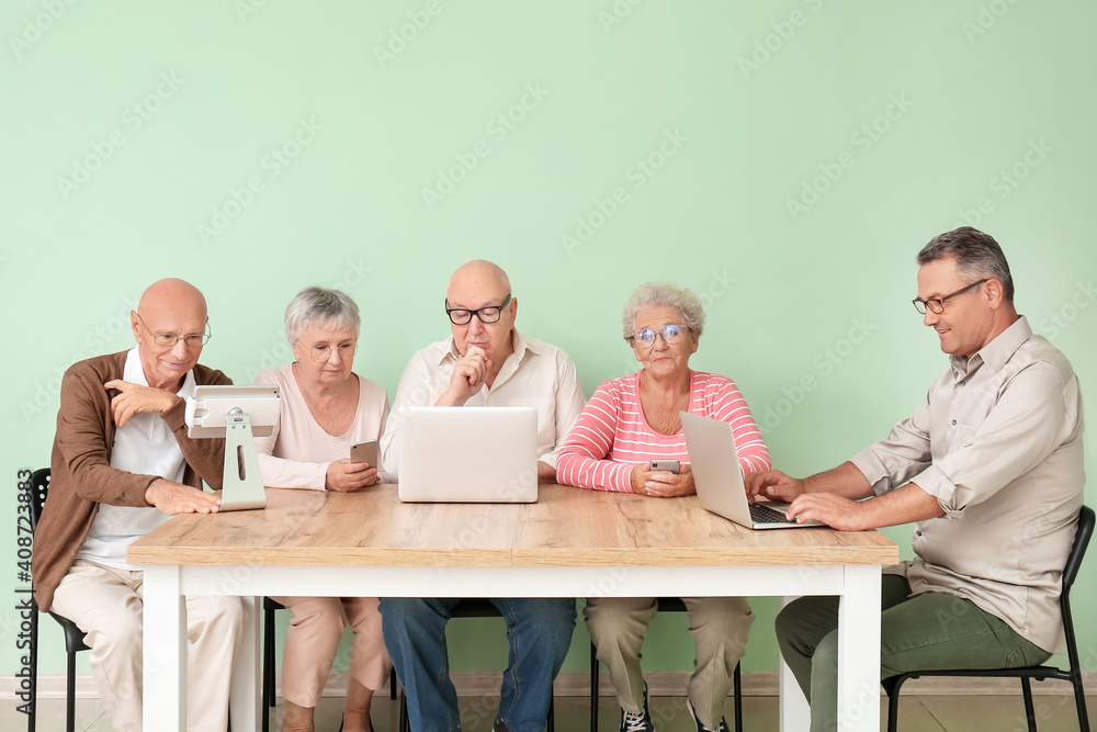 Senior people with different devices sitting at table in room