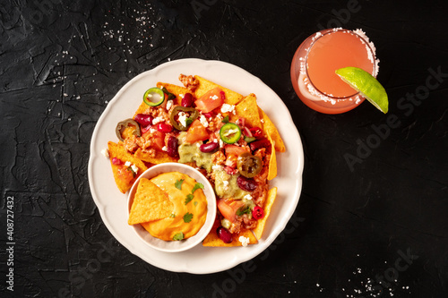 Mexican nachos with chili con carne and a Paloma cocktail, overhead shot on a black background © laplateresca