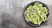 Sliced Cucumbers On A Round Plate On A Dark Gray Background. Top View, Flat Lay