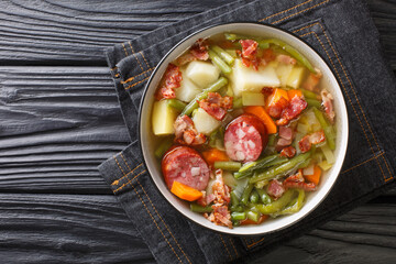 Sticker - Homemade soup of green beans, potatoes, leeks, carrots with sausages and bacon close-up on a plate on the table. Horizontal top view from above