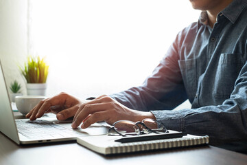 Close-up shot of man's hand using keyboard of laptop computer on office desk. He is working business in office with copy space. Business investment-finance accounting concept.