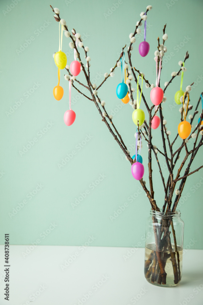 Stock-Foto „Bunte Ostereier an Osterstrauß aus Zweigen von Sal-Weide mit Weidenkätzchen Kätzchen vor Pastell Grün Hintergrund zu Ostern“