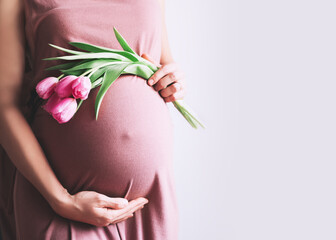 Beautiful pregnant woman with tulips flowers holds hands on belly. Young woman in dress waiting for baby birth. Pregnancy, Motherhood, Mother's Day Holiday concept.