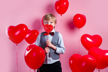 Wall Mural - Valentines day. Little cute boy eating candy on red heart balloons background