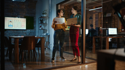 Aufkleber - Two Diverse Multiethnic Female Have a Discussion in Meeting Room Behind Glass Walls in an Agency. Creative Director and Project Manager Compare Business Results on Laptop and App Designs in an Office.
