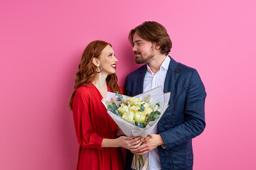 affectionate man offering his partner roses on pink background, lovely couple celebrating their anniversary, date or saint valentines day