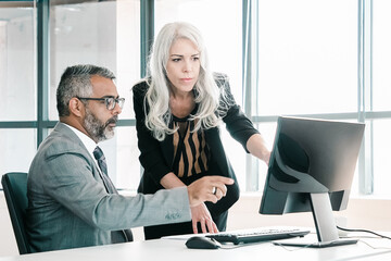 serious colleagues watching and discussing content on computer monitor, pointing at display and talk