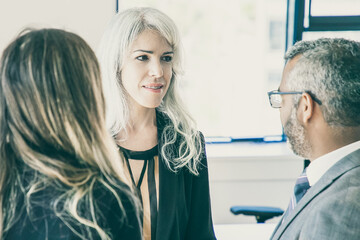 Wall Mural - Company managers wearing suits, standing in office, talking, discussing project. Medium shot. Business communication or briefing concept