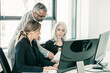 © Mangostar - Serious business group of three analyzing reports, sitting at workplace with monitors together, holding, reviewing and discussing papers. Copy space. Business meeting concept