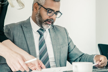 Wall Mural - Focused boss analyzing managers report, reading and reviewing papers while sitting at workplace. Business communication concept