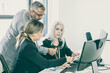 © Mangostar - Business team of three analyzing reports, sitting at workplace with monitors together, holding, reviewing and discussing papers with charts. Copy space. Inclusive workplace concept