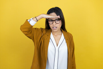 Young beautiful woman wearing a blazer over isolated yellow background very happy and smiling looking far away with hand over head. searching concept.