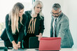 © Mangostar - Business group watching project presentation, standing at meeting table, looking at laptop display. Medium shot. Business communication concept