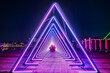 Purple coloured gate of light or purple light tunnel installation made of triangular neon and led lights at night as blurred people walk through the bright deep passage that resembles a human trachea