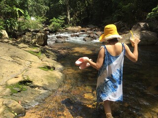 Wall Mural - A woman in a yellow hat is climbing a rock in the middle of the river.