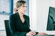 © Mangostar - Serious young businesswoman wearing jacket, using computer at workplace in office, typing and looking at display. Medium shot. Digital communication concept