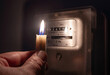 A person's hand with candle in complete darkness looking on electricity meter at home. Power outage, blackout concept.