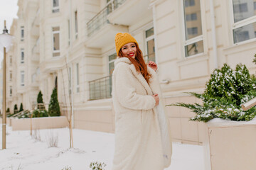 Wall Mural - Blithesome ginger girl in yellow hat smiling in january day. Outdoor photo of joyful red-haired female model in coat.