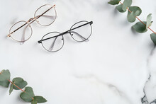 Woman's Eyeglasses And Eucalyptus Branches On Marble Background. Flat Lay, Top View.